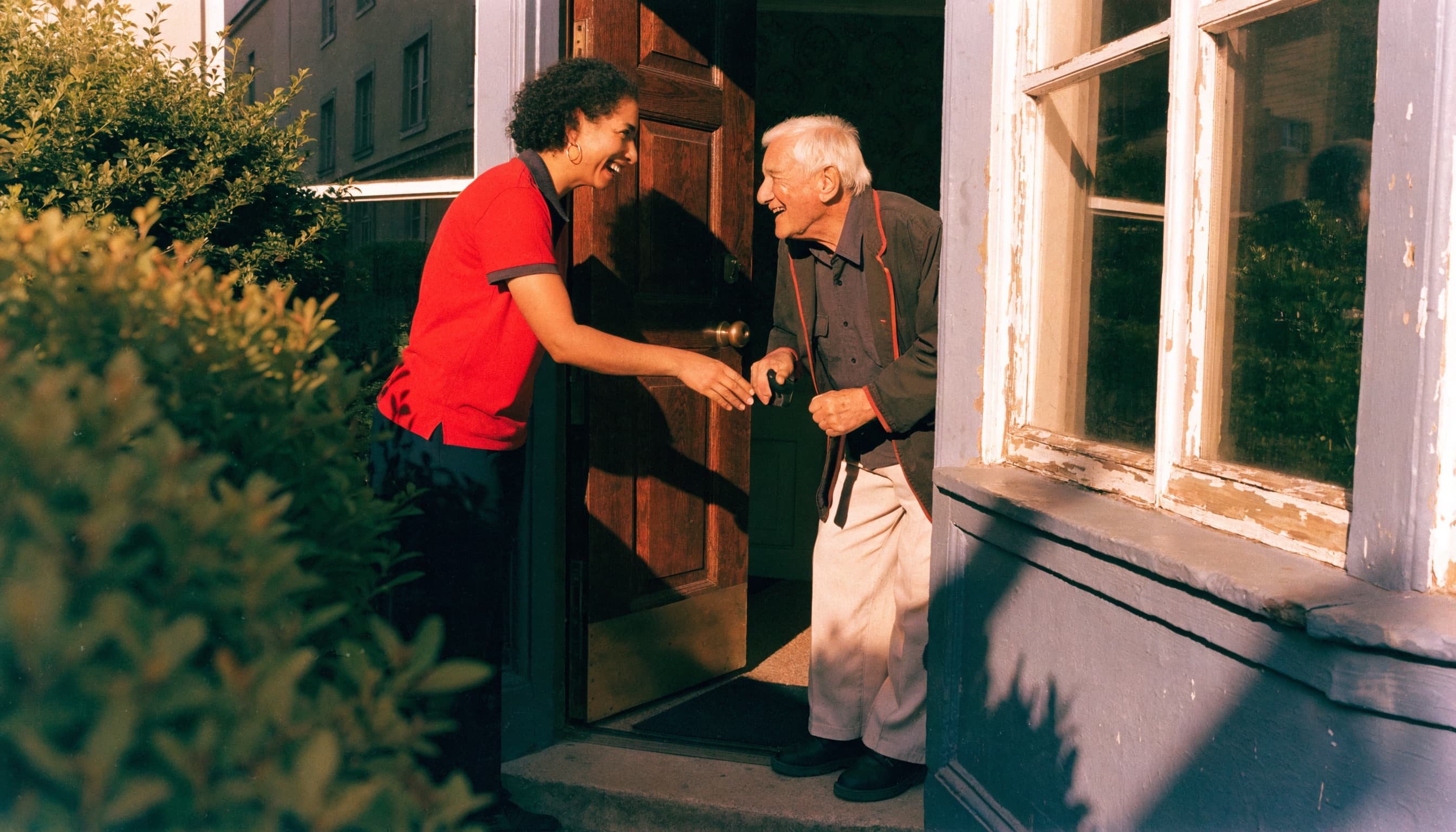 A home care worker warmly greeting an elderly man at his front door