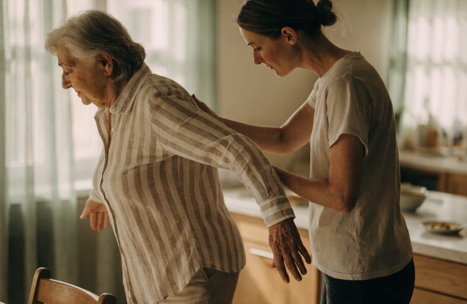 A physiotherapist supporting an older woman through a balance exercise at home
